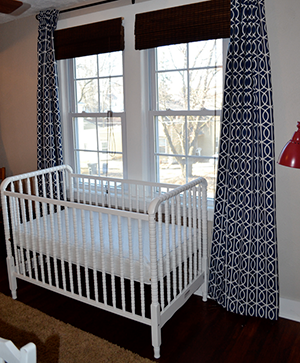 A crib by the window where there are window shades and curtains.